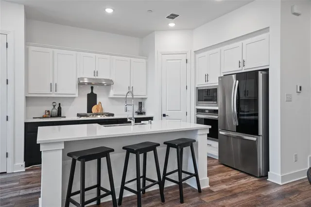 a kitchen with stainless steel appliances a sink a stove a refrigerator cabinets and wooden floor