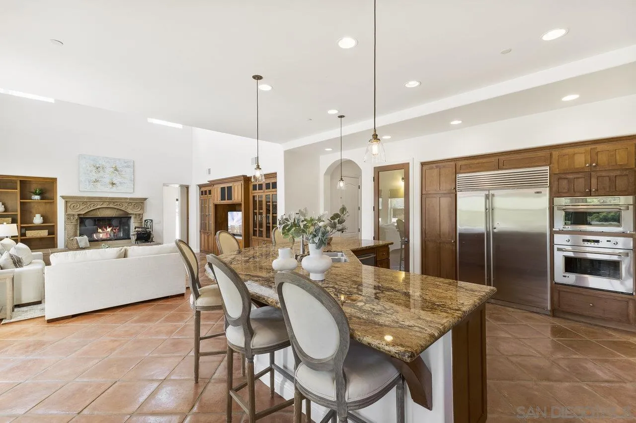 20919 Questhaven Road San Marcos, CA 92078 - Photo 16 of 54 a kitchen with stainless steel appliances granite countertop a kitchen island a stove a refrigerator a oven a sink a dining table and chairs with wooden floor