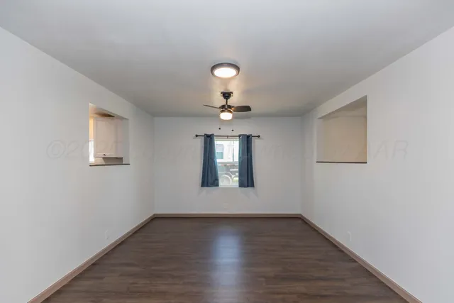 an empty room with wooden floor chandelier fan and windows