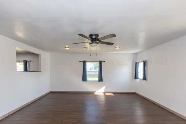 a view of an empty room with wooden floor and a ceiling fan