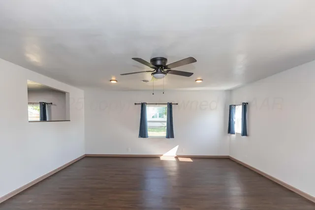 a view of an empty room with wooden floor and a ceiling fan