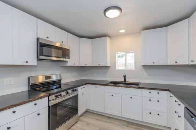 a kitchen with granite countertop white cabinets stainless steel appliances a sink and a window
