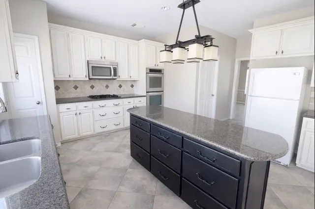 a kitchen with granite countertop a refrigerator a sink and white cabinets