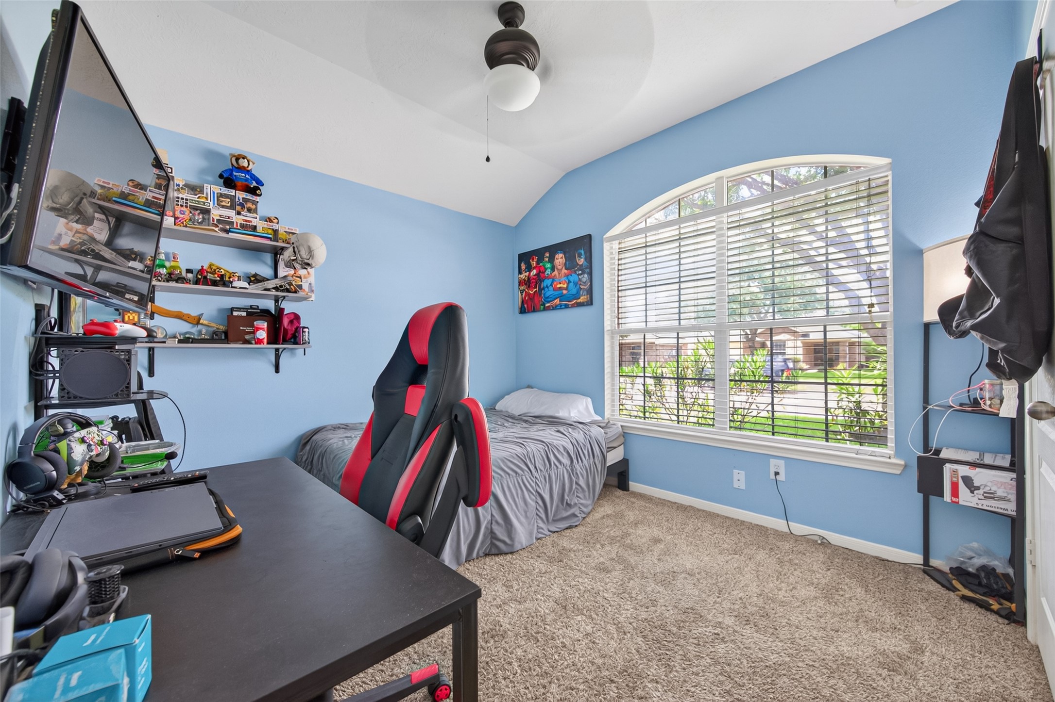 8622 Henrico Lane Rosenberg, TX 77469 - Photo 14 of 20 This cozy bedroom features a large arched window that provides plenty of natural light, soft blue walls, and carpeted flooring. The room includes a small bed, a desk with gaming accessories, and shelves for storage or display. Perfect for a child's room or home office.