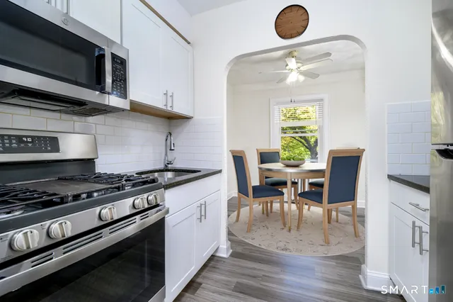 a kitchen with stainless steel appliances granite countertop a stove a sink dishwasher a dining table and chair with wooden floor