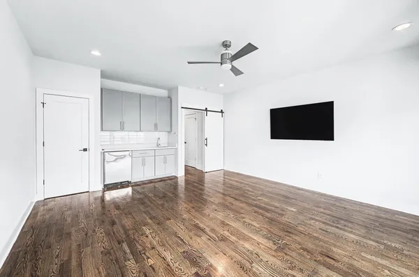 a view of an empty room with wooden floor and a kitchen