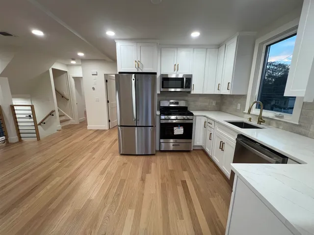 a kitchen with granite countertop a refrigerator a sink dishwasher and a stove with wooden floor
