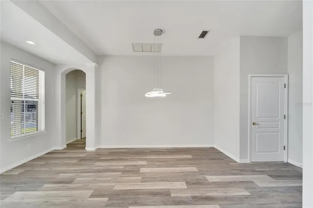 an empty room with chandelier fan and windows