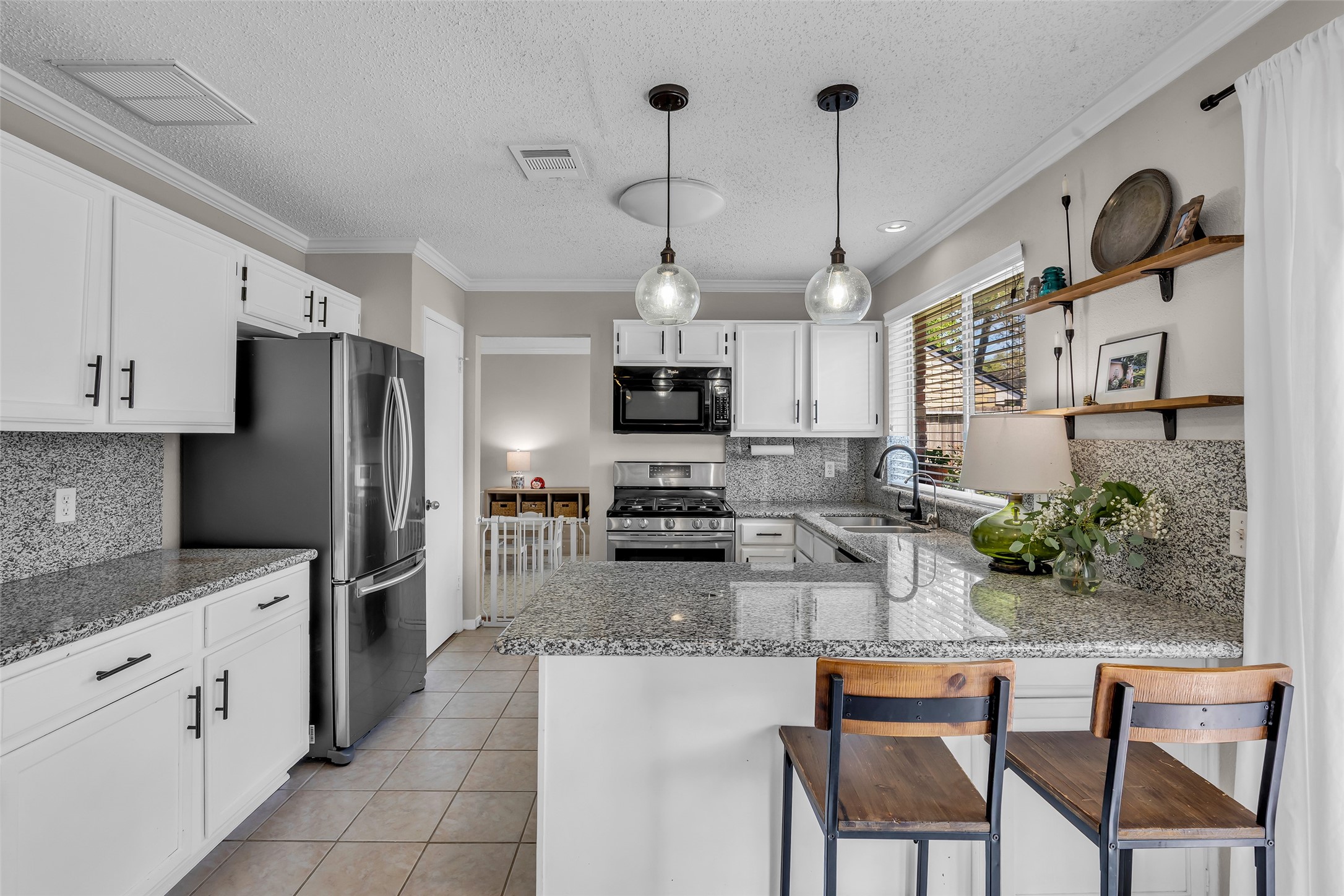 9415 Towerstone Drive Spring, TX 77379 - Photo 15 of 44 This kitchen features modern stainless steel appliances, granite countertops, and white cabinetry. A window above the sink offers natural light, while open shelving and sleek fixtures provide a contemporary touch.