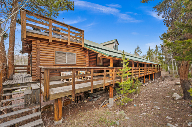 4725 Pine Ridge Road Evanston, UT 82930 - Photo 60 of 82 Log cabin exterior featuring a second-story balcony, a wrap-around wooden deck, a prominent dormer, a metal roof, and a woodland setting