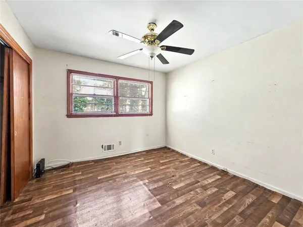an empty room with wooden floor fan and windows