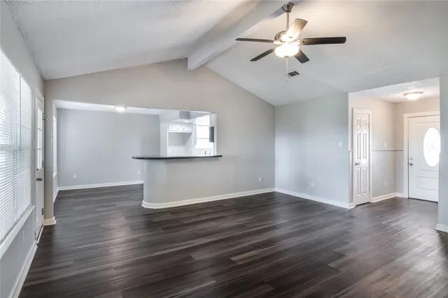 a view of an empty room with wooden floor and a ceiling fan