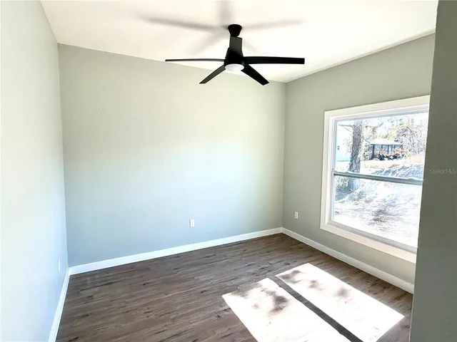 an empty room with wooden floor fan and windows