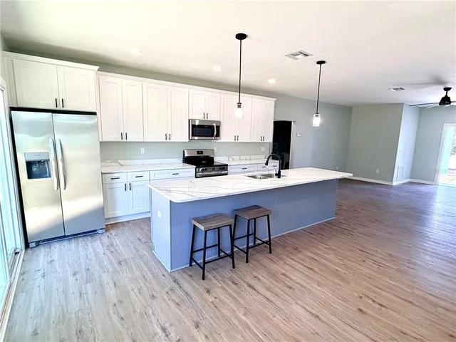 a kitchen with stainless steel appliances a sink a stove a refrigerator a center island and wooden floor