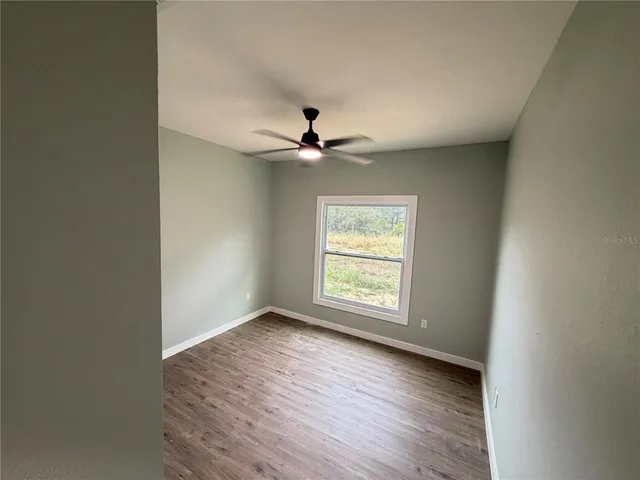 an empty room with wooden floor ceiling fan and windows