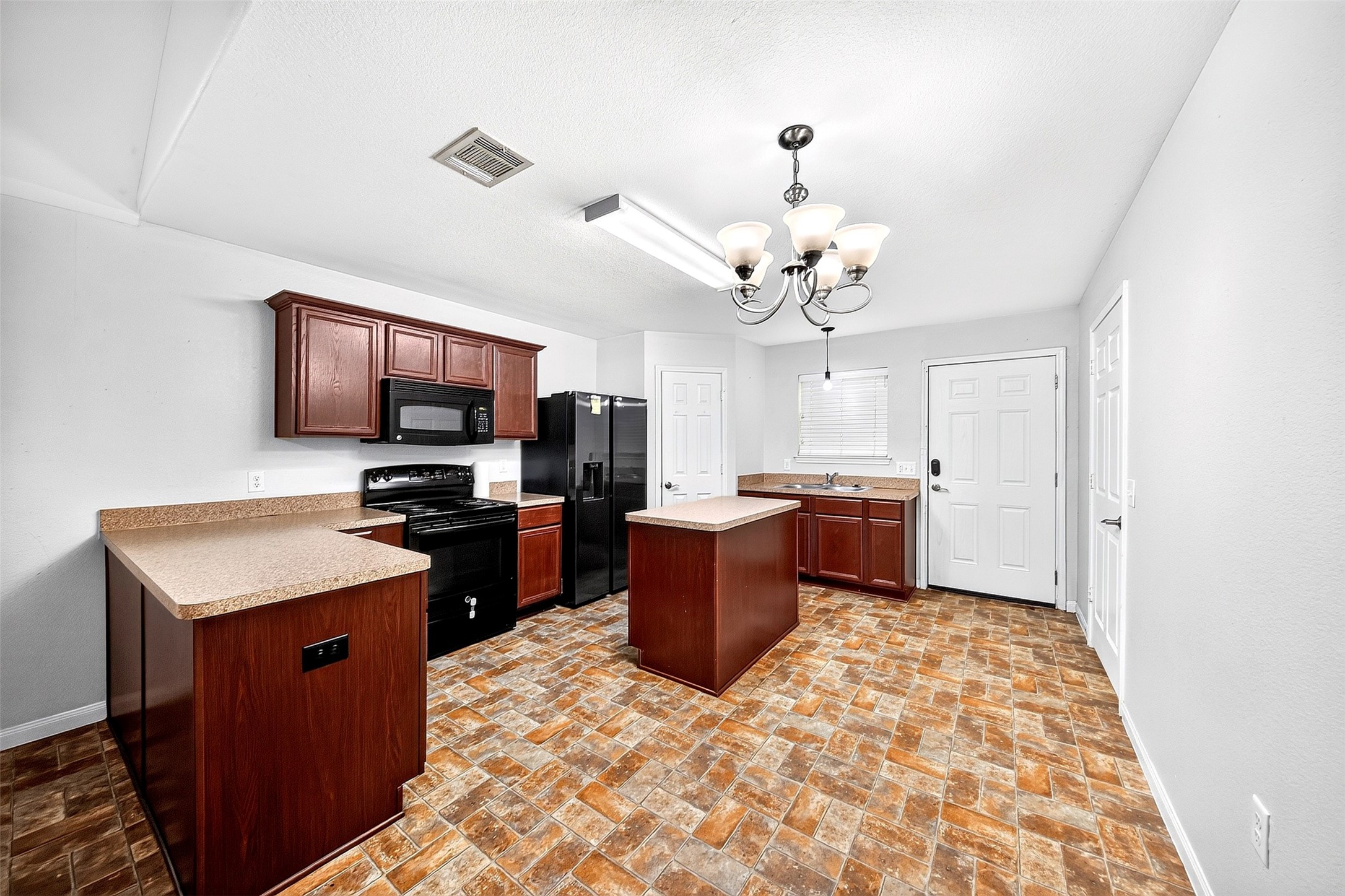 148 Fear Road Winnie, TX 77665 - Photo 8 of 34 This spacious kitchen features rich wooden cabinetry, a large center island, and modern black appliances. The room is well-lit with a stylish chandelier and ample natural light, complemented by a warm, patterned tile floor.