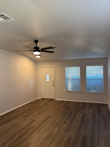 an empty room with wooden floor chandelier fan and windows