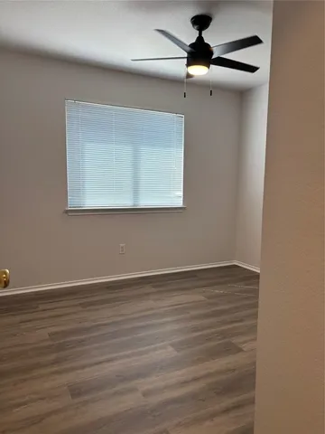 a view of an empty room with wooden floor ceiling fan and window