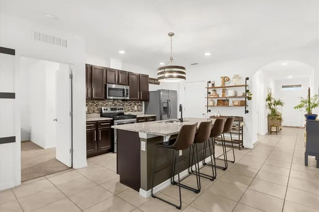 a kitchen with stainless steel appliances kitchen island granite countertop a refrigerator a stove a sink a dining table and chairs with wooden floor