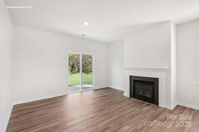 a view of an empty room with wooden floor fireplace and a window