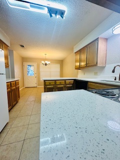 102 Verna Spur, Unit A Georgetown, TX 78628 - Photo 20 of 20 Kitchen with light countertops, a peninsula, light tile patterned floors, freestanding refrigerator, and a textured ceiling