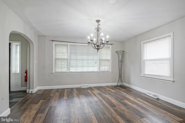 an empty room with wooden floor chandelier and windows