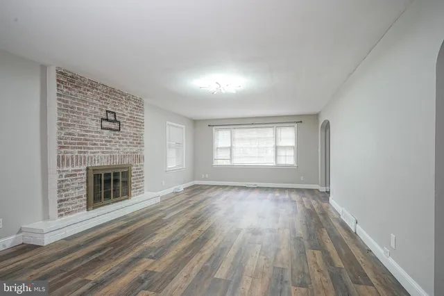 an empty room with wooden floor fireplace and windows