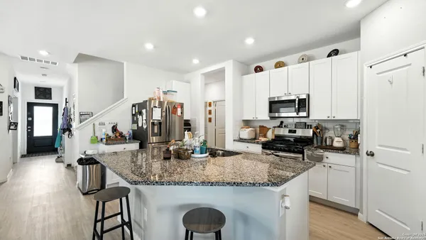 a kitchen with stainless steel appliances kitchen island granite countertop a stove top oven a sink dishwasher a dining table and chairs with wooden floor