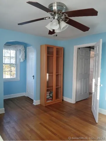 an empty room with wooden floor chandelier fan and windows
