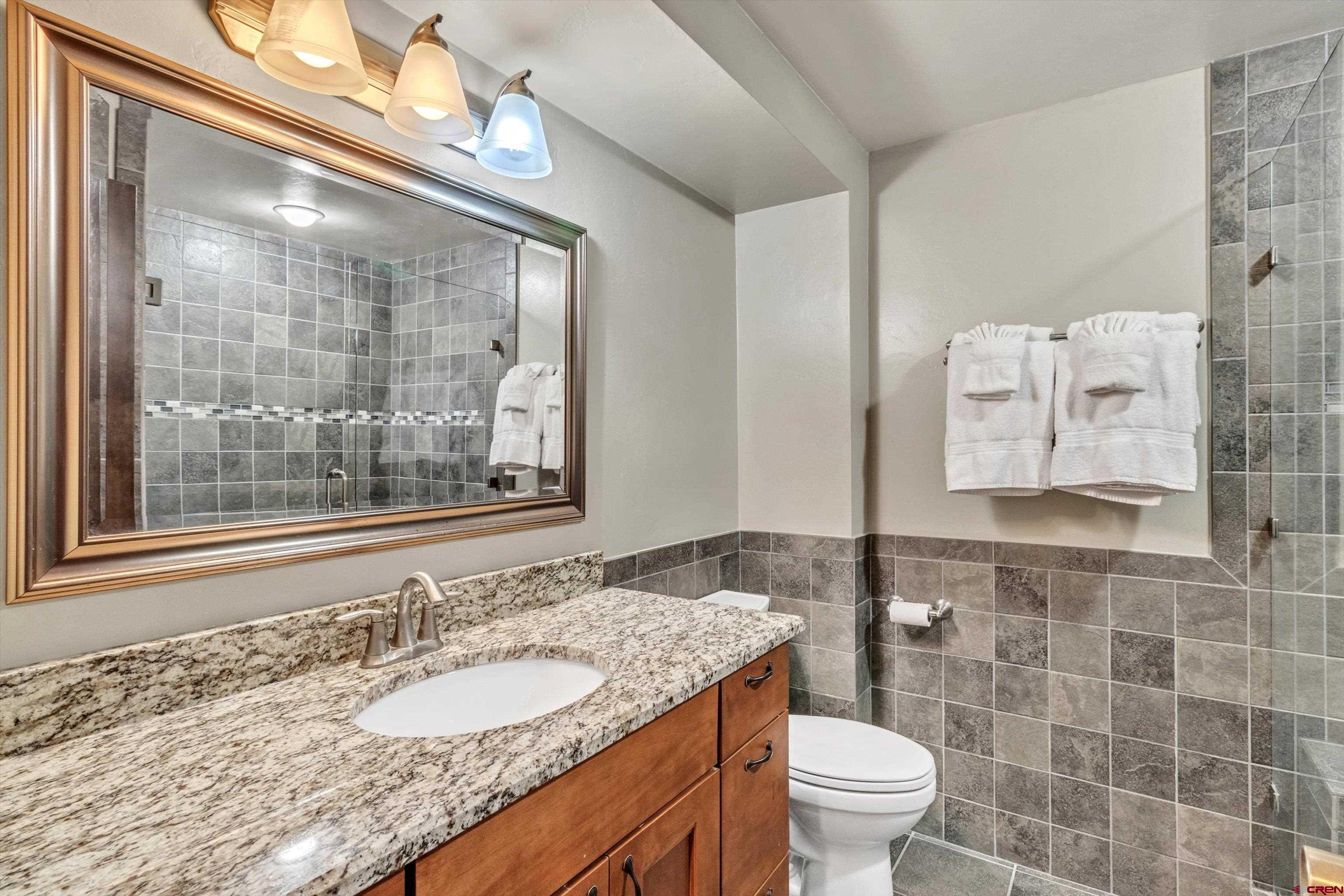 314 Tamarron Drive, Unit 511 Durango, CO 81301 - Photo 19 of 36 a bathroom with a granite countertop toilet a sink a mirror and a shower