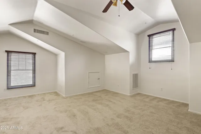 an empty room with chandelier fan and windows