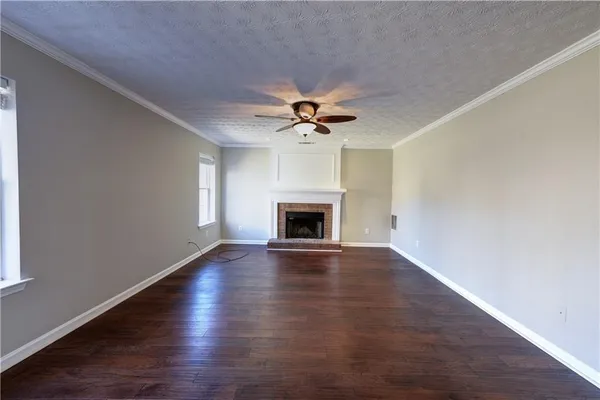 an empty room with wooden floor a ceiling fan a fireplace and windows