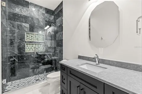 a bathroom with a granite countertop sink a toilet a mirror and shower