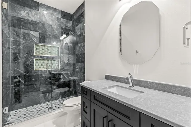a bathroom with a granite countertop sink a toilet a mirror and shower
