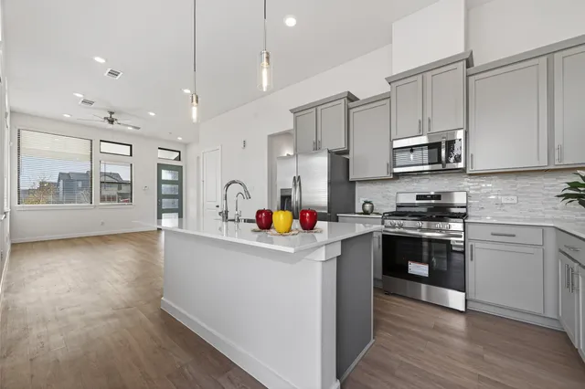 a kitchen with stainless steel appliances granite countertop a stove top oven a sink dishwasher and white cabinets with wooden floor