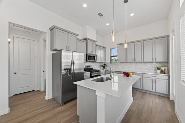 a kitchen with stainless steel appliances a refrigerator stove a sink and white cabinets with wooden floor