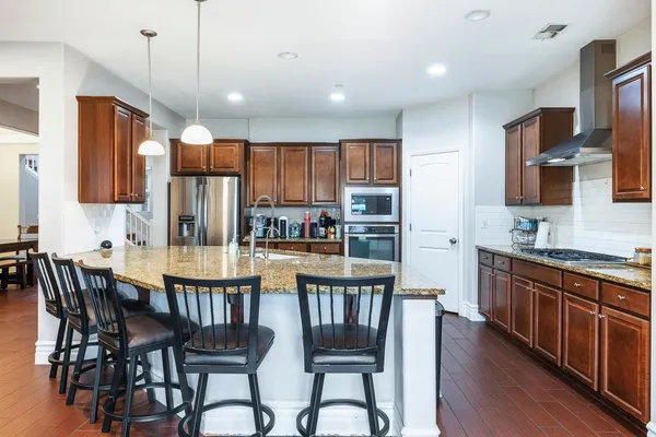 a kitchen with stainless steel appliances kitchen island granite countertop a dining table chairs sink and cabinets