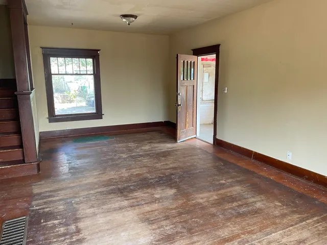 a view of an empty room with wooden floor and a window