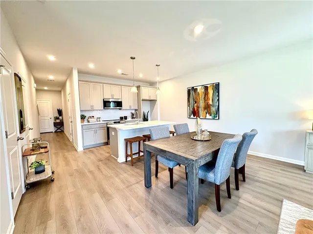 a kitchen with stainless steel appliances kitchen island granite countertop a stove a sink a microwave a dining table and chairs with wooden floor