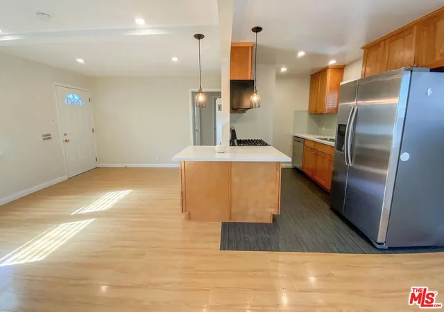 a view of an empty room with wooden floor and a kitchen