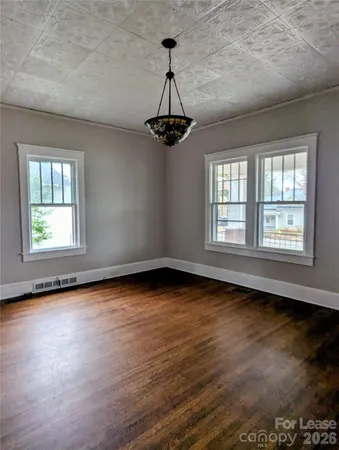 an empty room with wooden floor chandelier fan and windows