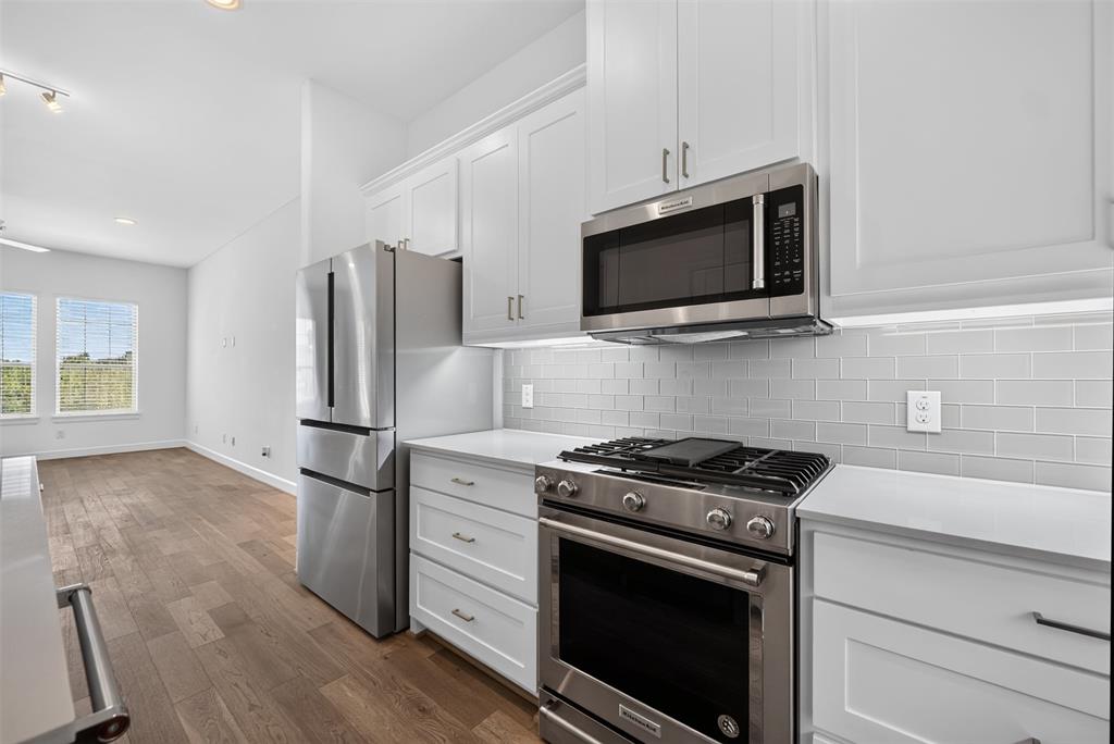 5015 Meridian Lane, Unit 2102 Addison, TX 75001 - Photo 11 of 36 Modern kitchen featuring white shaker cabinetry, stainless steel appliances, light gray subway tile backsplash, and light-toned countertops