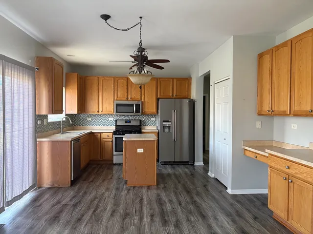 a kitchen with stainless steel appliances granite countertop a refrigerator a sink dishwasher a stove and white countertops with wooden floor