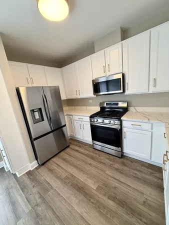a kitchen with granite countertop a refrigerator a stove top oven and white cabinets