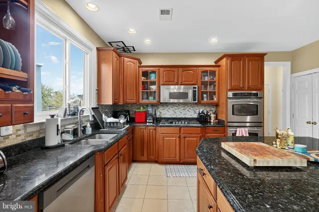 a kitchen with stainless steel appliances granite countertop a sink dishwasher a refrigerator and a dining table with the living room view