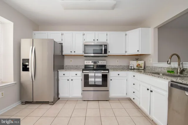 a kitchen with granite countertop a refrigerator stove and white cabinets