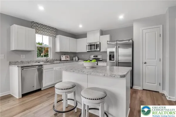 a kitchen with stainless steel appliances granite countertop a refrigerator a sink dishwasher a stove and white cabinets with wooden floor