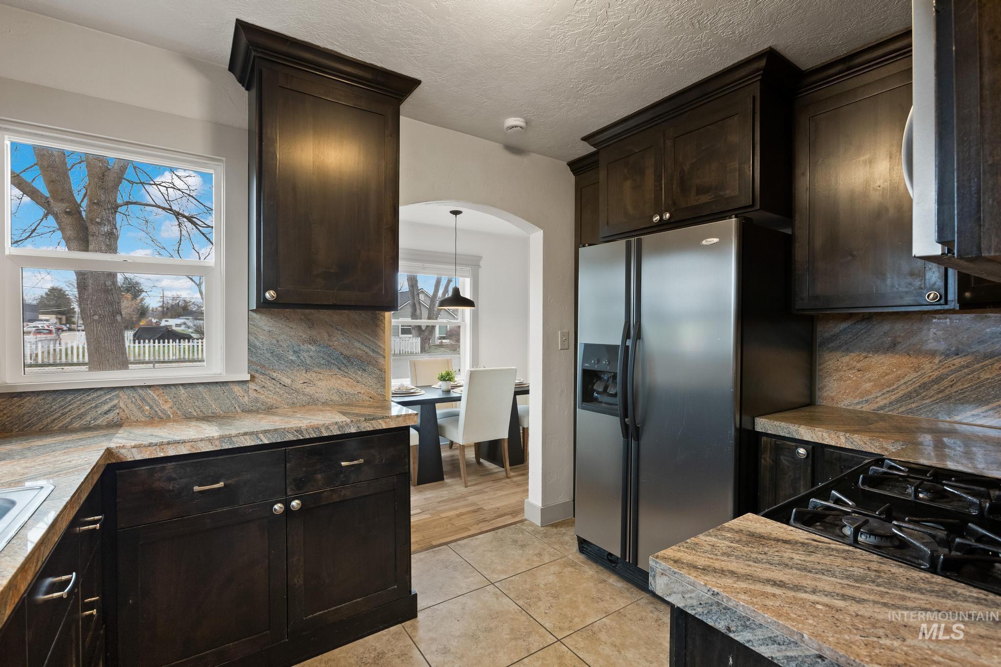 1019 North 30th Street Boise, ID 83702 - Photo 12 of 26 Kitchen with dark brown cabinets, backsplash, stainless steel fridge, light tile patterned flooring, and arched walkways