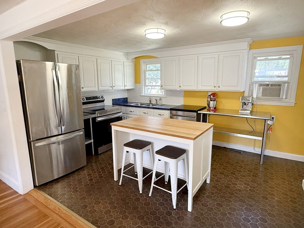 11 Webb Road Sharon, MA 02067 - Photo 7 of 19 a kitchen with stainless steel appliances granite countertop a stove a refrigerator a microwave a dining table and chairs with wooden floor