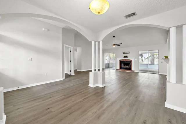 an empty room with wooden floor fireplace cabinet and windows
